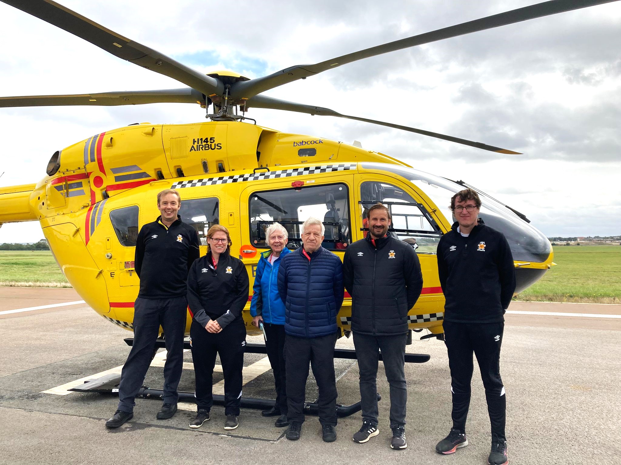 Patient Allan and staff from Cambridge United on a base visit in from of the EAAA helicopter.