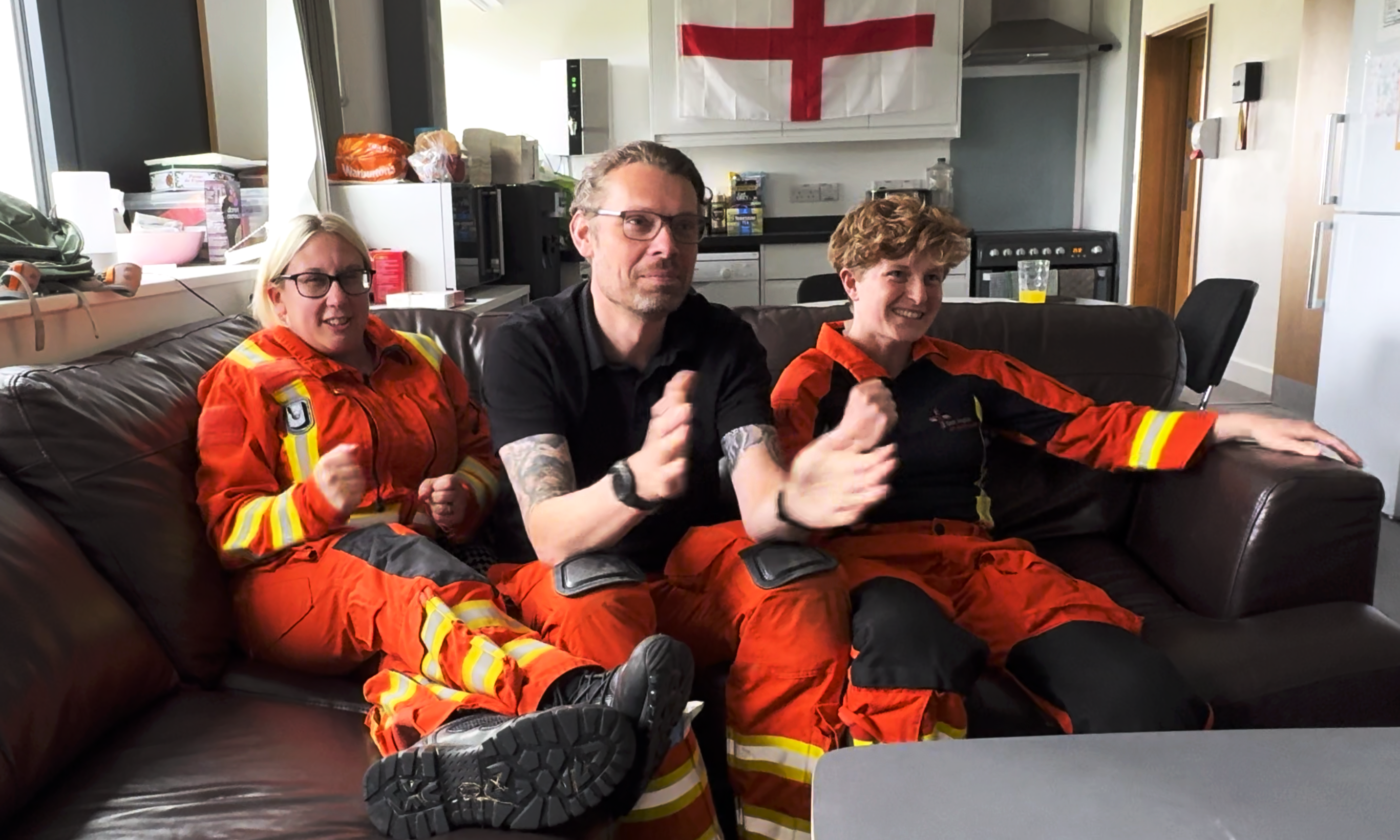 3 members of the EAAA crew on sofa cheering as they watch a football match on TV