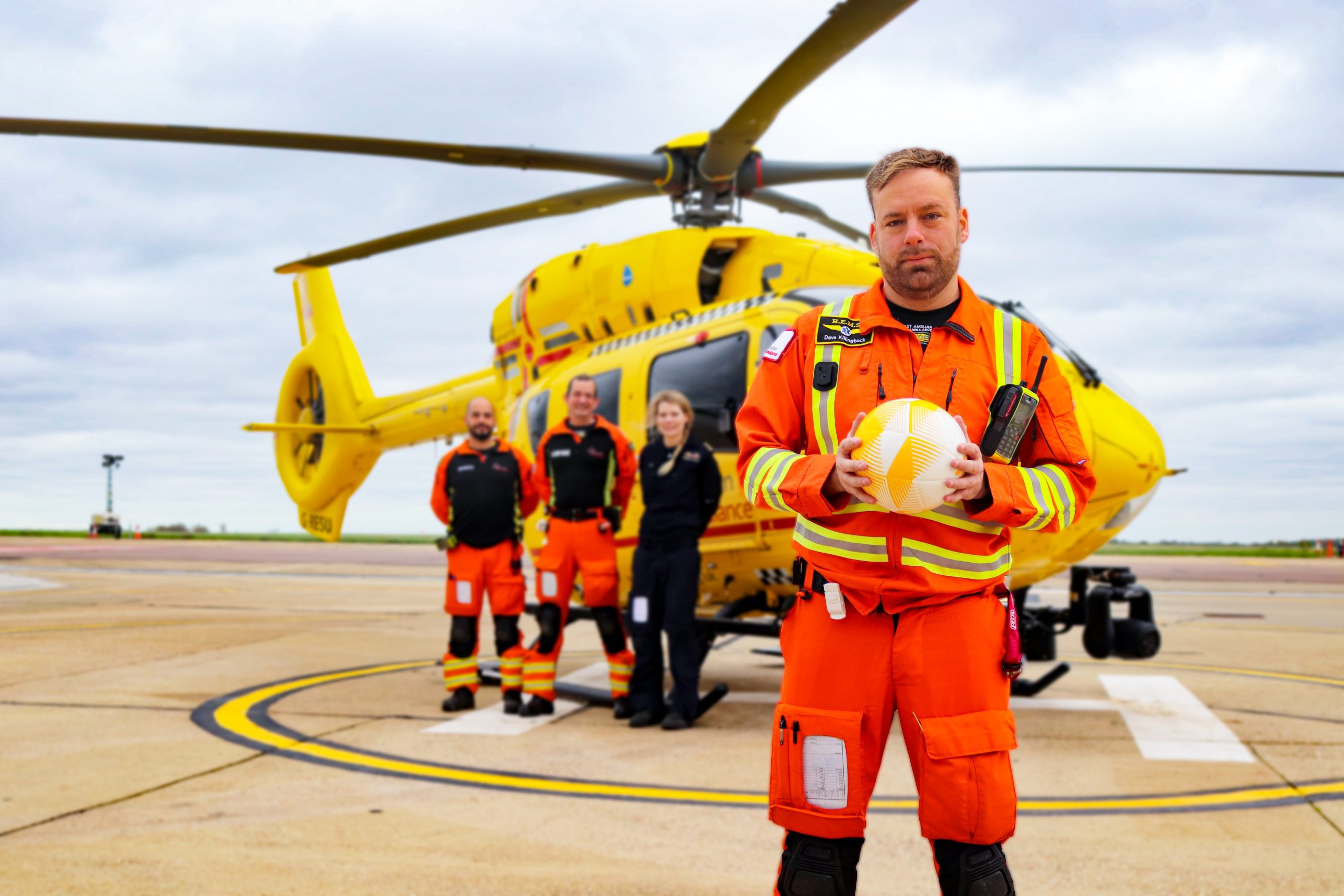 Crew member holding football in front of EAAA, yellow helicopter