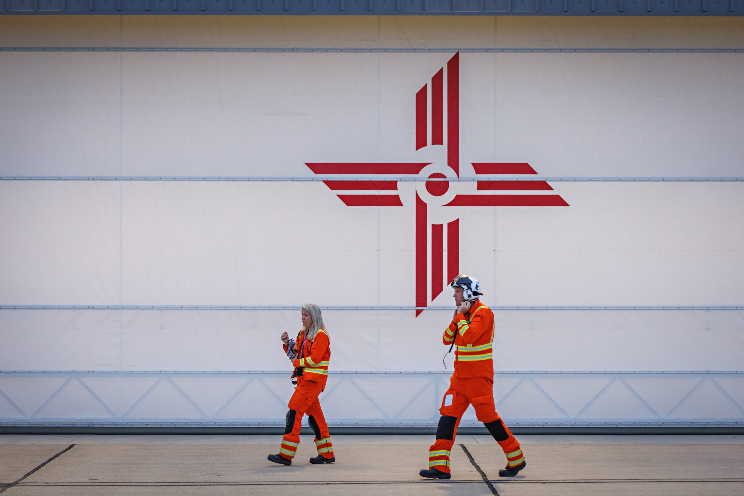 EAAA crew in orange flight suits and holding helmets walking across helipad