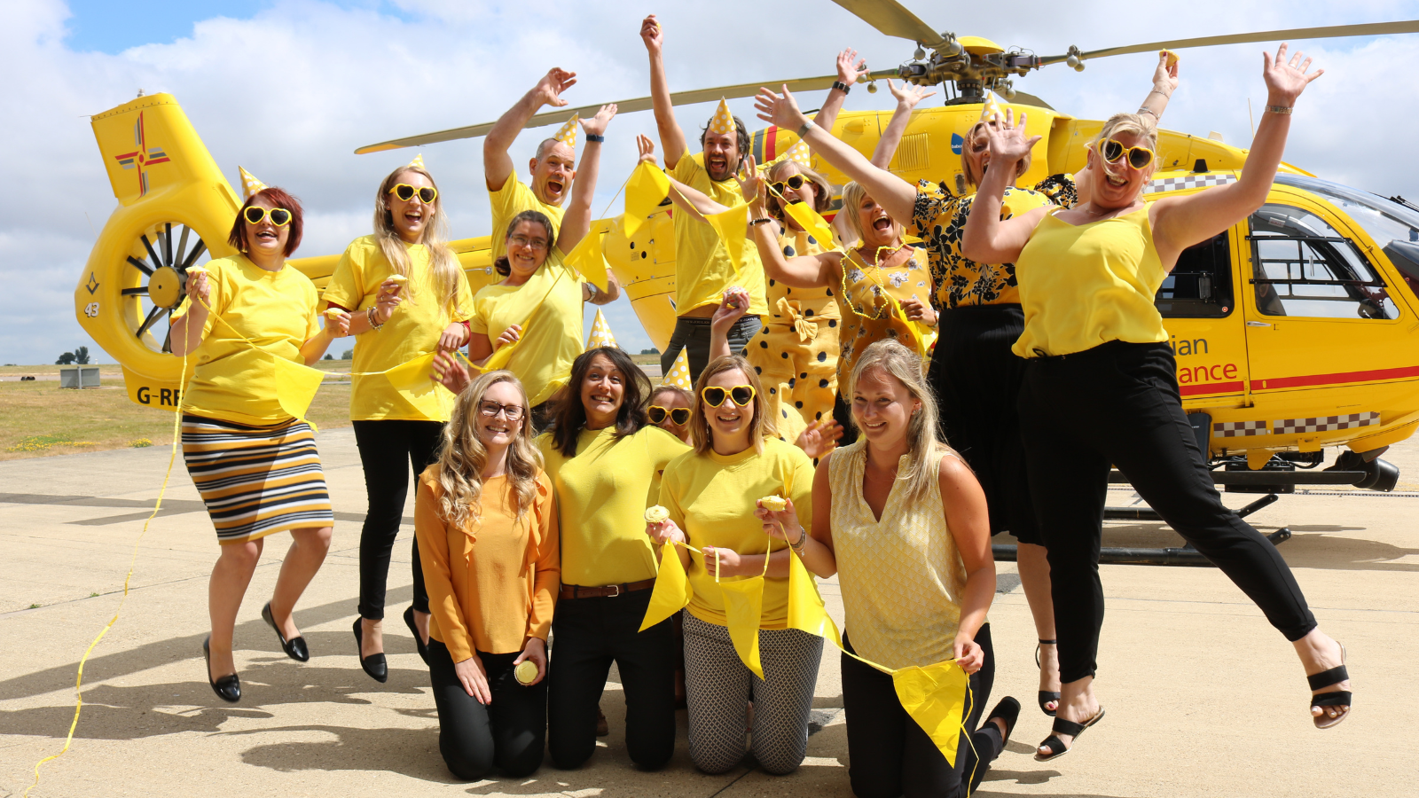 Group of people taking part in EAAA's 'Get Up and Go Yellow' and wearing yellow in front of yellow helicopter