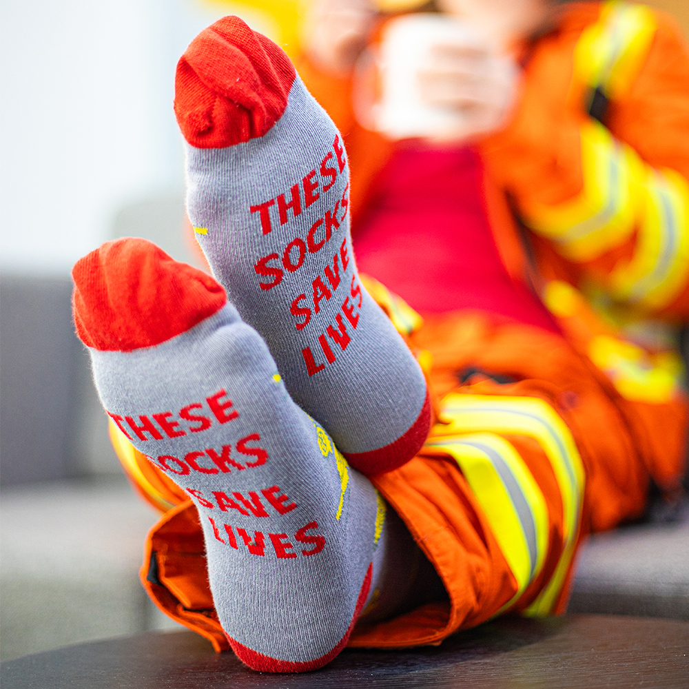 Crew member wearing grey and red East Anglian Air Ambulance socks with 'These socks save lives' on the sole of foot