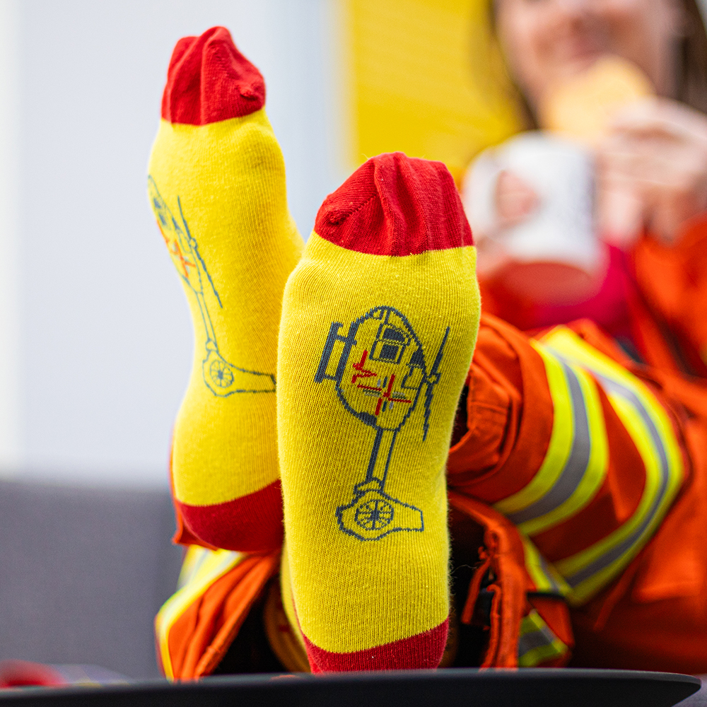 Crew member wearing yellow and red East Anglian Air Ambulance socks with helicopters on the sole of foot