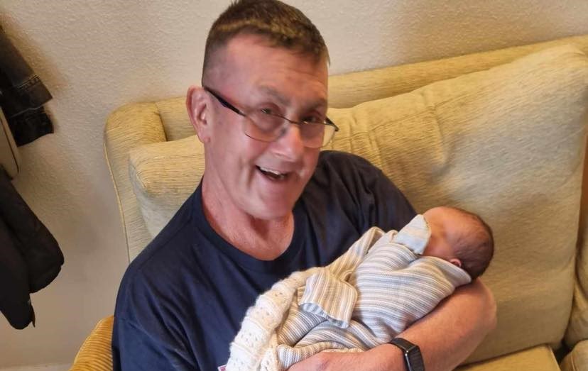 Steve Varney holding his latest grandchild after his incident.