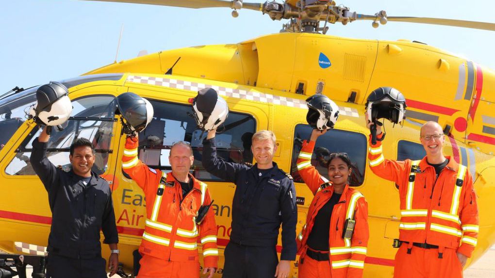 Crew with helmets off in front of helicopter